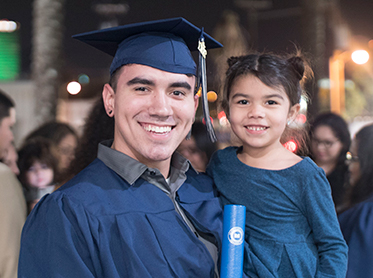 DMC graduate in cap and gown with his young daughter